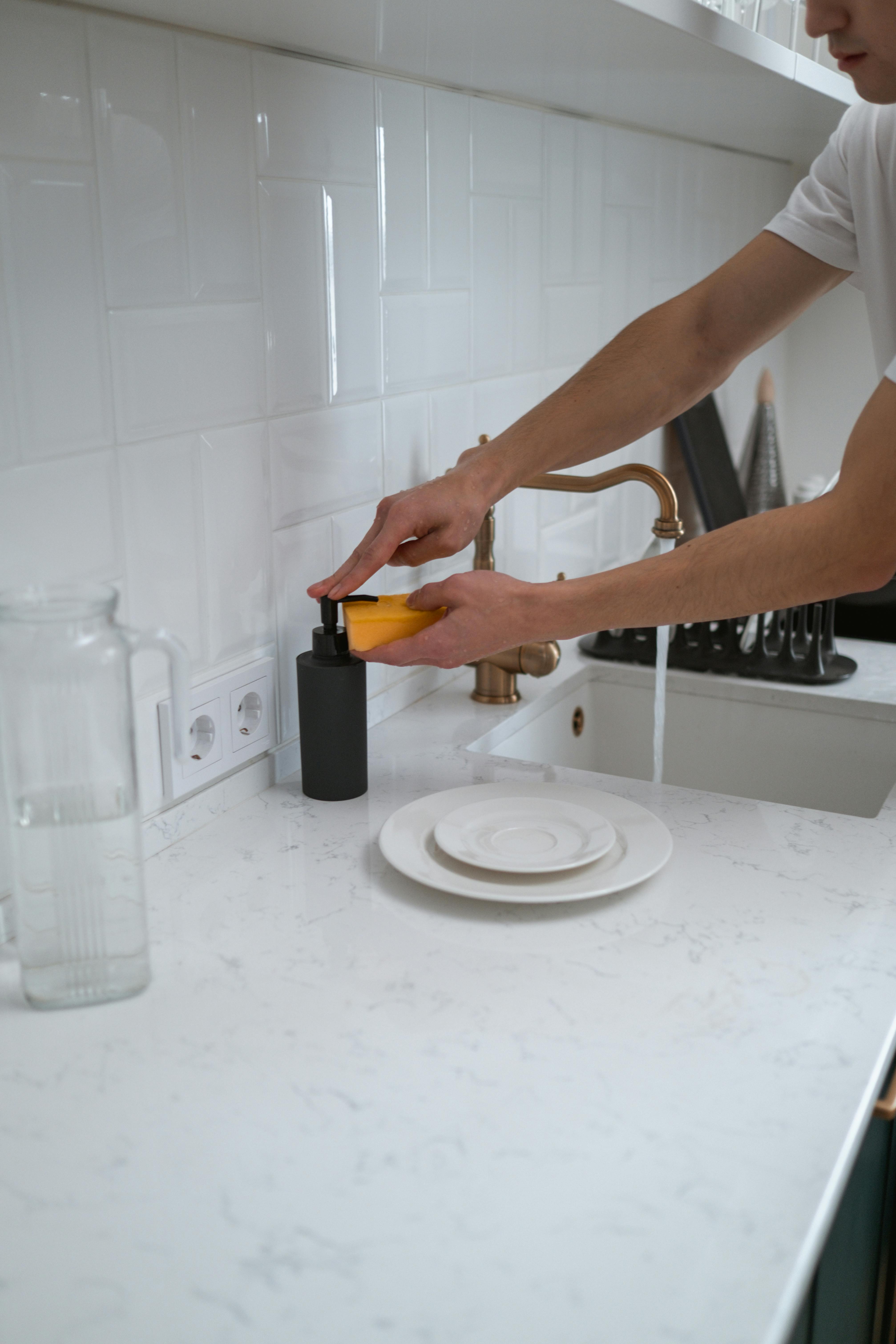 Washing dishes with soap and sponge at a kitchen sink during everyday food-safe cleaning